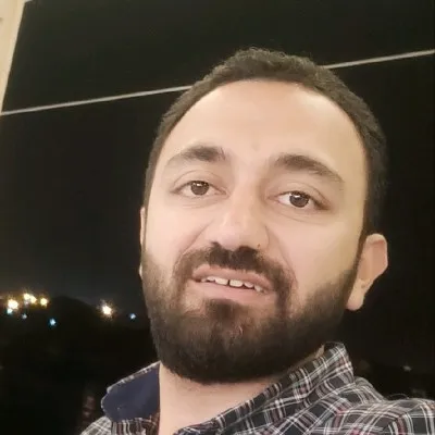 A young woman with long hair smiles while standing against a green backdrop, wearing a casual dark sweater.